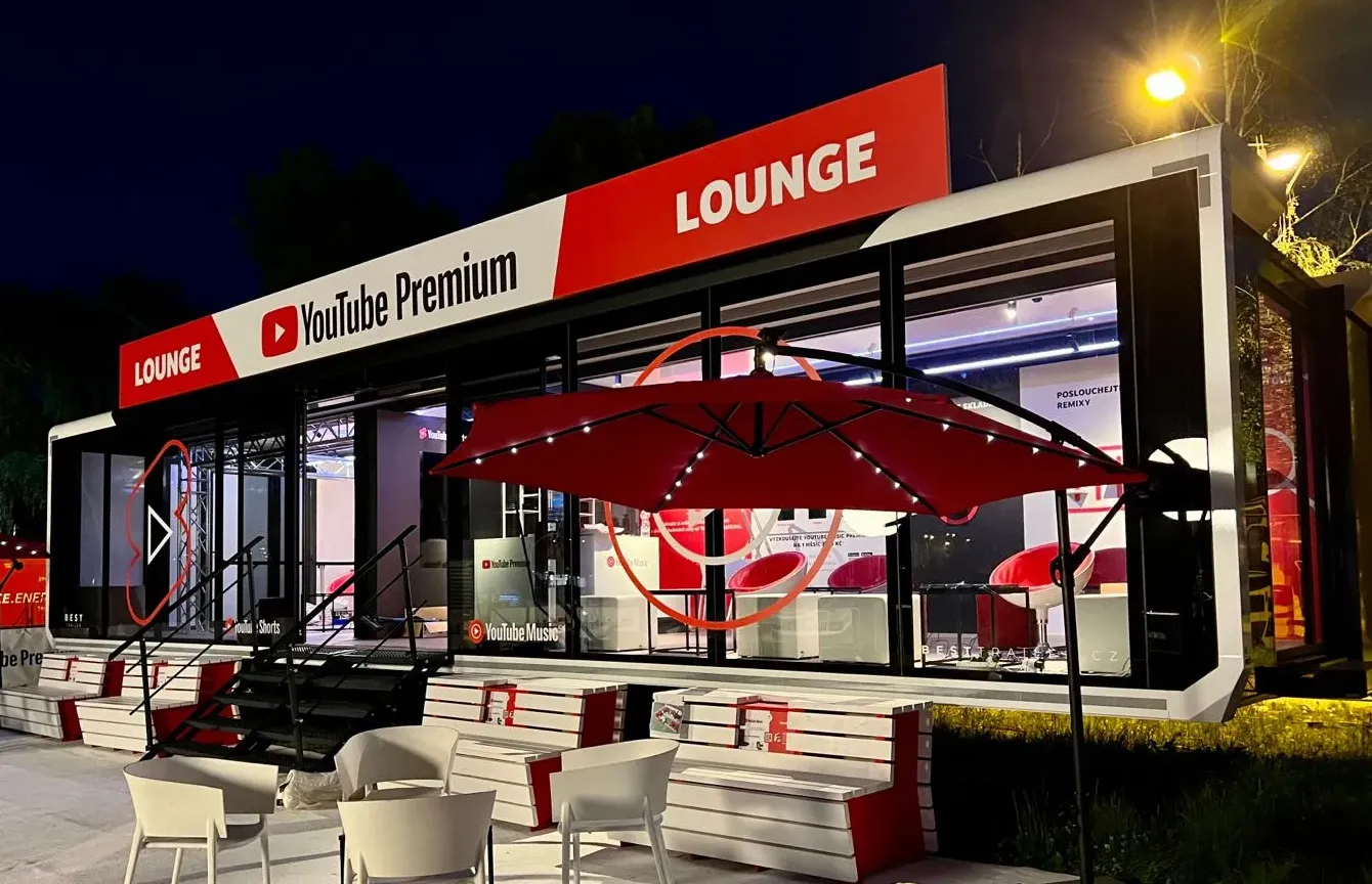 A YouTube event trailer at night, featuring a area with red umbrellas and furniture.